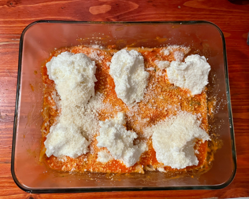 A pan with half pasta and sauce, with six scoops of ricotta cheese evenly spread out.